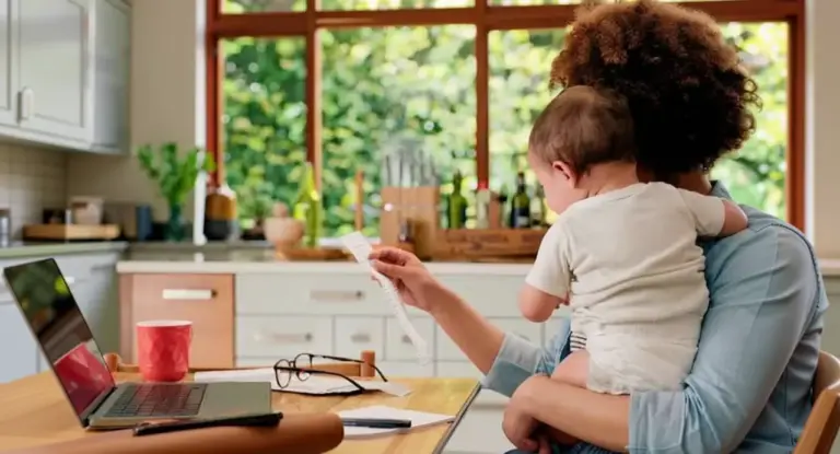 Una persona con un bambino in braccio lavora al computer in cucina