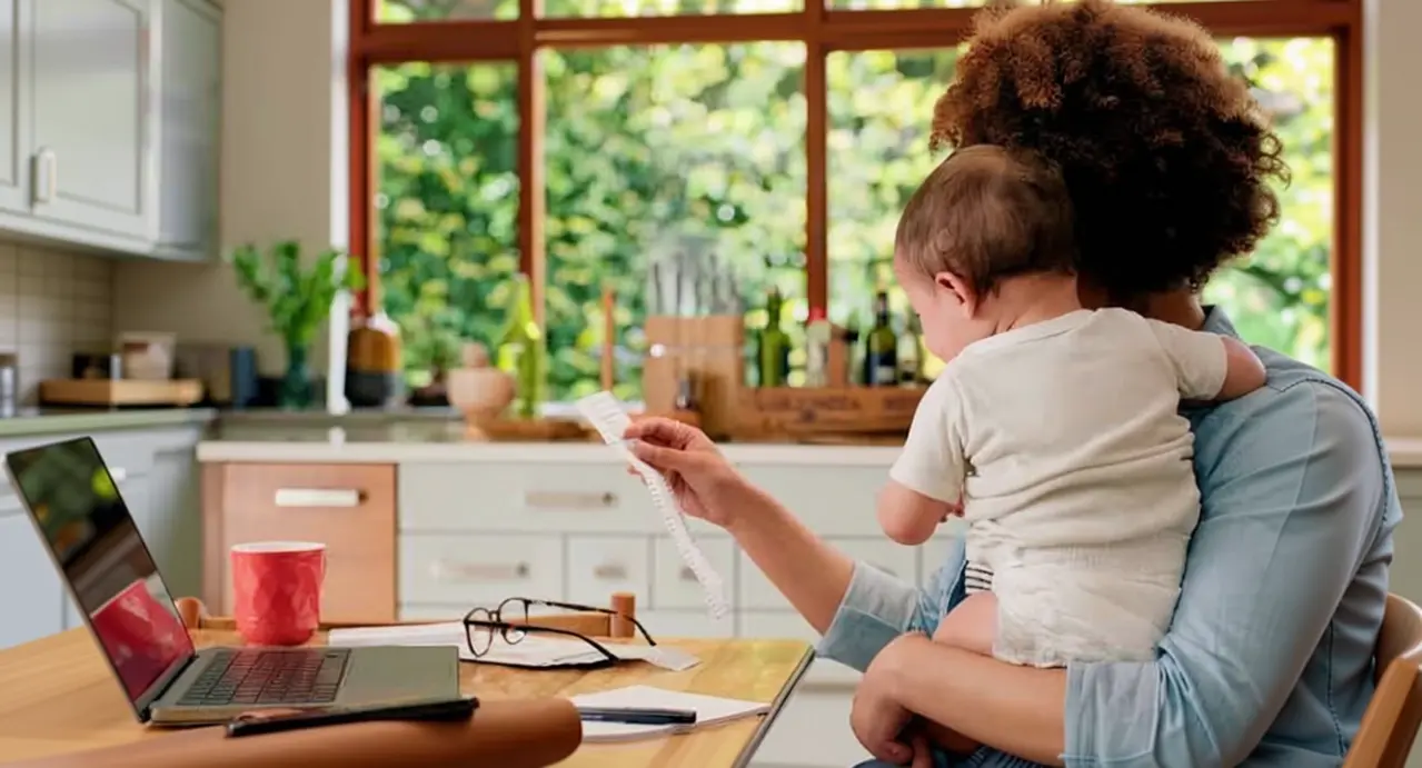 Una persona con un bambino in braccio lavora al computer in cucina