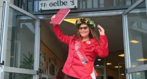 Una giovane laureata gioiosa con corona d’alloro e tesi in mano davanti all’ingresso di un edificio