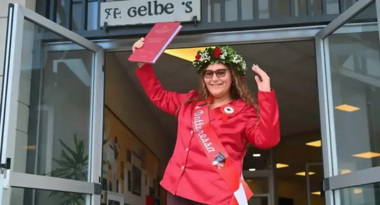 Una giovane laureata gioiosa con corona d’alloro e tesi in mano davanti all’ingresso di un edificio