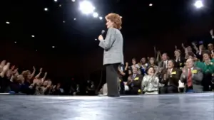 Una persona con microfono sul palco davanti a un pubblico applaudente in uno studio televisivo