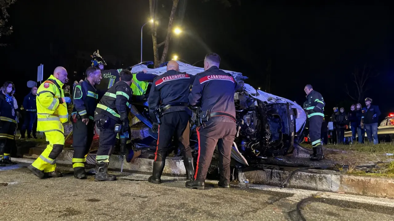 Soccorritori e carabinieri attorno a un'auto distrutta dopo un grave incidente notturno a Roma