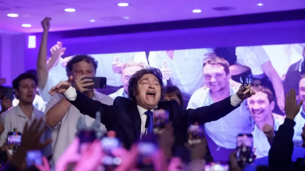 Un uomo in giacca e cravatta esulta davanti a una folla durante un comizio elettorale