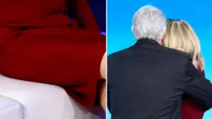 Due persone si abbracciano durante una trasmissione televisiva, una indossa un abito rosso.