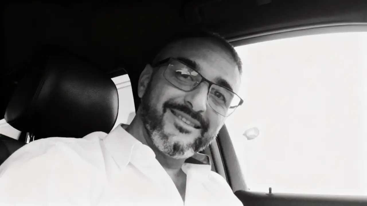 Un uomo con occhiali e barba corta sorride seduto all'interno di un'auto