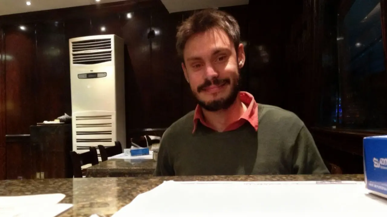 Un uomo seduto in un locale con pareti scure e un climatizzatore sullo sfondo