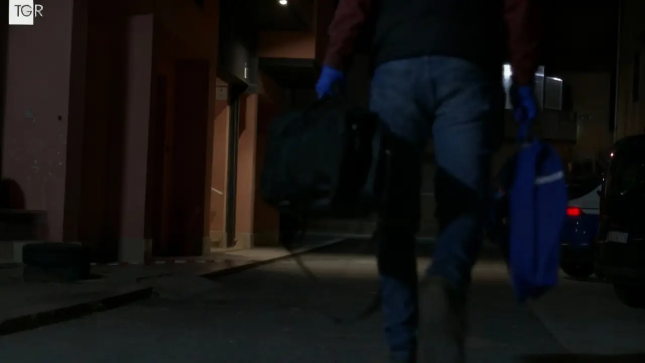 Persona con guanti blu cammina di notte portando due borse in una strada urbana