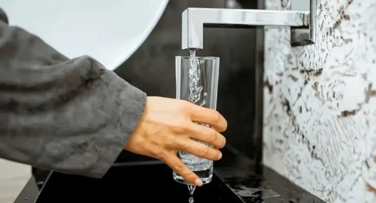 Una mano riempie un bicchiere con acqua da un rubinetto moderno