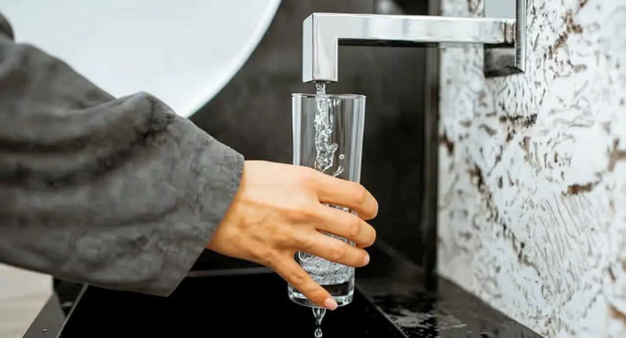 Una mano riempie un bicchiere con acqua da un rubinetto moderno