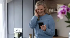 Donna sorridente guarda il telefono in cucina