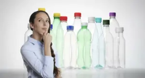 Donna pensierosa davanti a bottiglie di plastica con tappi colorati non rimovibili