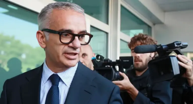 Un uomo in giacca e cravatta parla davanti a una videocamera e giornalisti fuori da un edificio