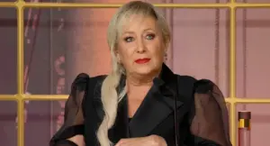 Una donna con capelli biondi seduta a un tavolo mentre parla al microfono