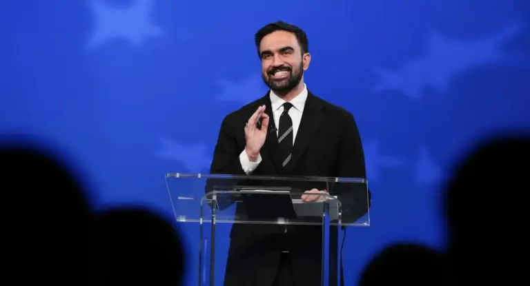 Una persona in abito formale parla da un podio su sfondo blu con stelle.