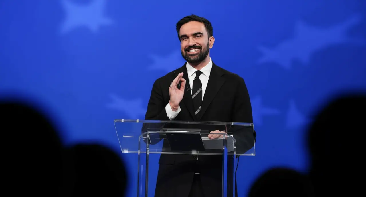 Una persona in abito formale parla da un podio su sfondo blu con stelle.